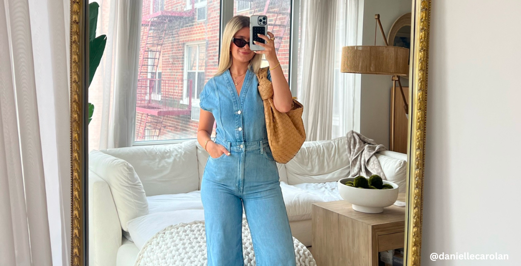 Social media influencer posing in living room mirror in a denim jumpsuit with a tan leather handbag