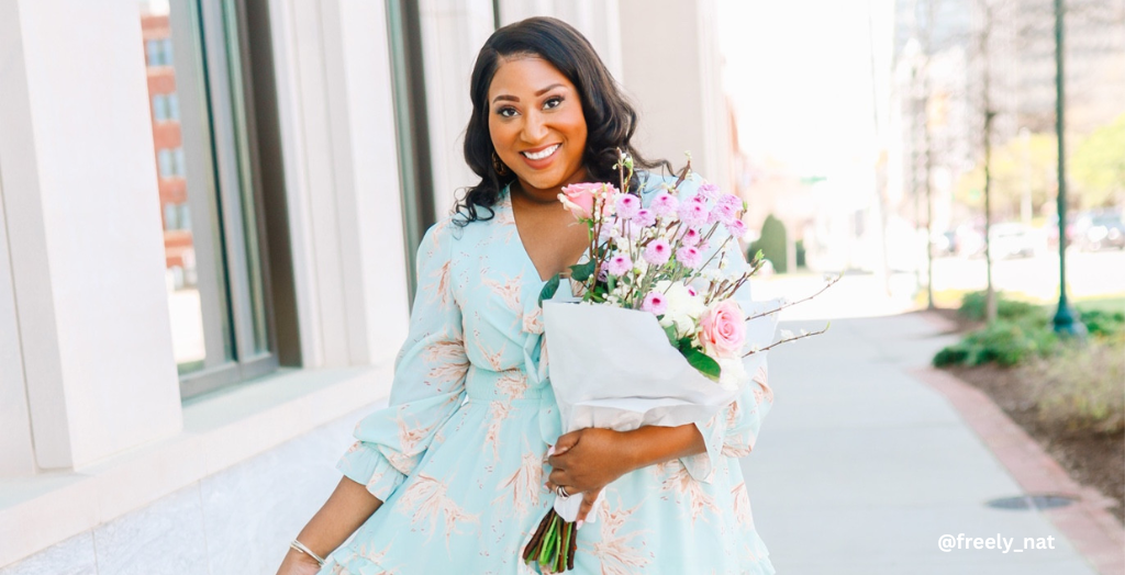 Content creator and influencer @freely_nat holding a bouquet of pink flowers in a light blue tea-length dress. 