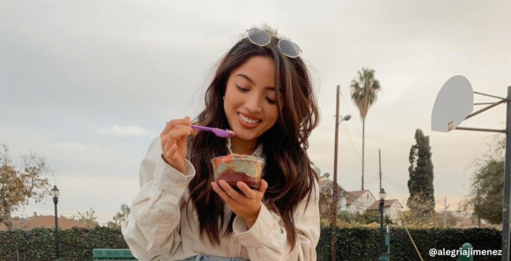Influencer @alegriajimenez smiles while eating an acai smoothie bowl. 