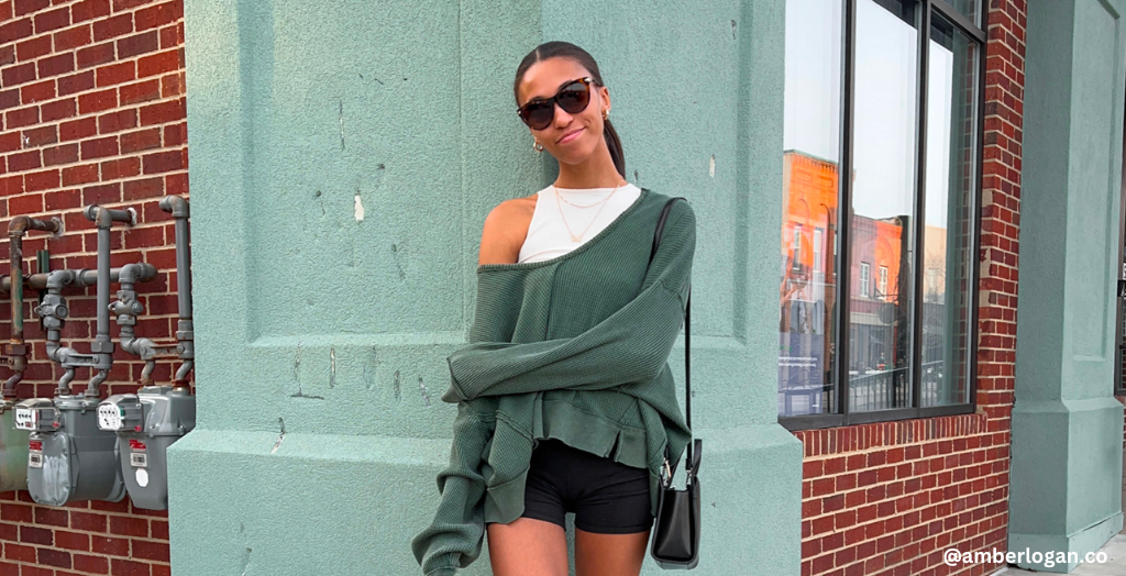 Social media influencer posing in a green sweater with a black leather handbag